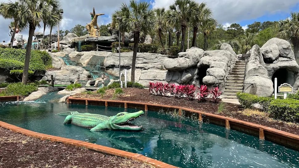 A crocodile in the water below the rock formations and waterfalls at Captain Hook's Adventure Golf